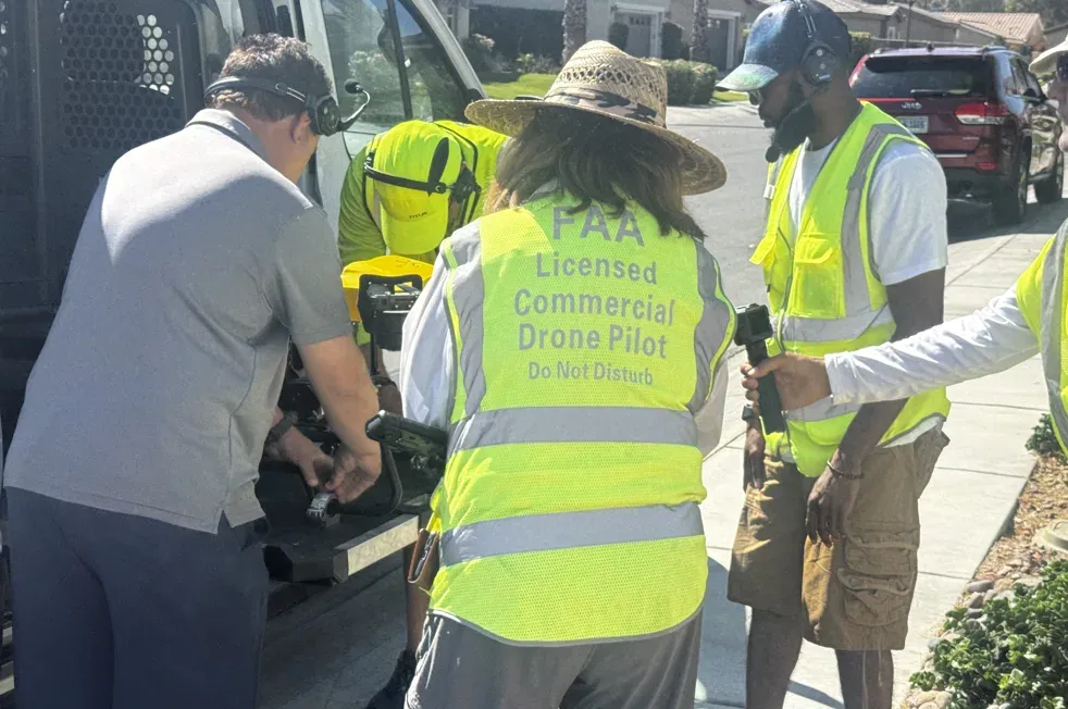 DronePower1's FAA-licensed commercial drone crew prepping equipment on a Coachella Valley job site, headsets on and high-visibility vests marked FAA Licensed Commercial Drone Pilot